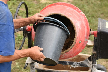 Water is being poured from a black bucket into a red concrete mixer filled with clay. Construction...