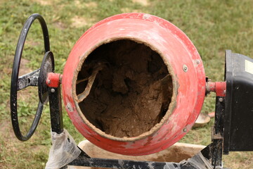 Red concrete mixer with clay mixing inside, placed on green grass outdoors. Concept of...
