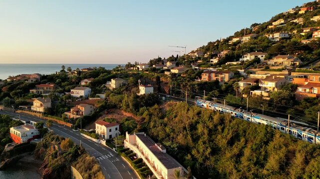 Aerial cinematic view of a train crossing the Antheor Viaduct in the Esterel Mountains near Saint Raphael, French Riviera, overlooking the Mediterranean Sea and luxury villas along the Cote dAzur at s