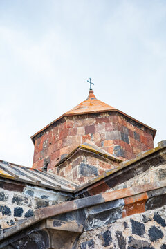 Close-up architectural view of the historic Sevanavank Monastery dome in Armenia, showcasing its red and black volcanic tuff stones topped with a Christian cross