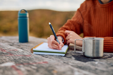 Person journaling or sketching in a spiral notebook, enjoying a hot cup of coffee or tea while camping or hiking