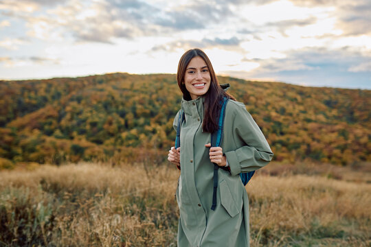 Young woman with backpack enjoying outdoors and fresh air, traveling in nature during fall season. Smiling at camera