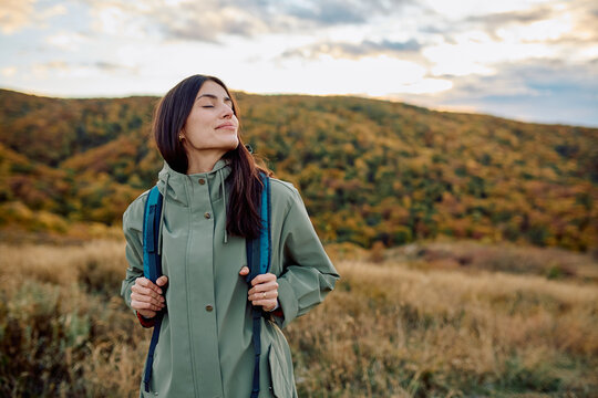 Woman with eyes closed, enjoying fresh air and tranquility while hiking in peaceful autumn nature with mountains in background