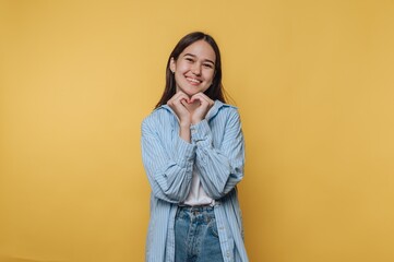Smiling woman making a heart shape with hands on yellow background.