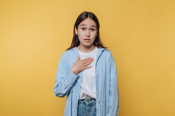 A young woman with a surprised expression, hand on chest, against a yellow background.