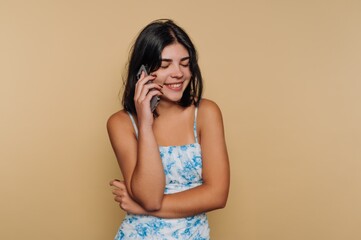 Obraz premium Young woman smiling while talking on a phone against a beige background.