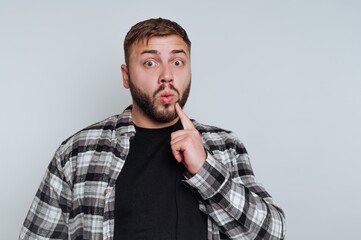 Obraz premium Man with surprised expression, wearing plaid shirt, finger on lips.