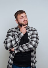 Fototapeta premium Man in plaid shirt pondering with hand on chin against gray background.