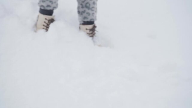 close-up of a child's feet walking in the snow, slow steps child walking in the snow,in white boots little girl walking in the snow