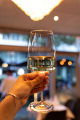 Hand Holding White Wine Glass Under Chandelier