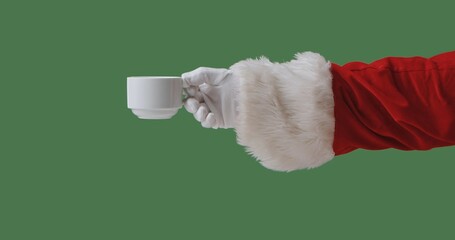 Santa hand in a red suit with a white fur cuff and glove holding a cup of coffee isolated on a green background. Perfect for Christmas banners, cards, and holiday advertising.