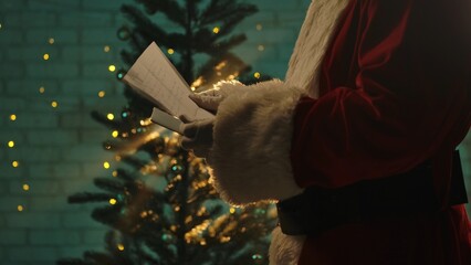 Santa Claus reads a wish list in front of a beautifully lit Christmas tree, capturing festive...