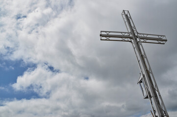 Fototapeta premium Steel lattice cross on top of a mountain against a blue sky and clouds