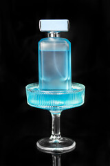 Blue bottle of eau de toilette in a cocktail glass with blue ice on a dark background