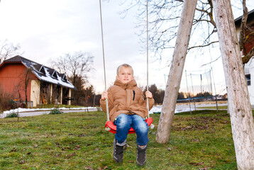 Young caucasian boy on red swing outdoors in winter coat