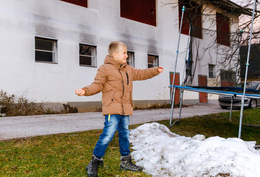 Caucasian young boy playing outdoors in winter wearing brown jacket near trampoline
