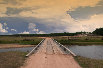 Old wooden bridge over the river. Landscape with cloudy sky.
