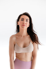 Fototapeta premium Sports woman standing in activewear with abs muscles, looking at camera isolated on white background. Caucasian 30s fitness girl wears beige top and pink leggings. Slim fit brunette with blue eyes.