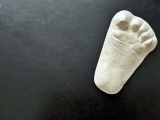 White plaster footprint sculpture rests on dark textured surface, highlighting craftsmanship and artistic detail, creating a striking visual contrast and minimalist aesthetic
