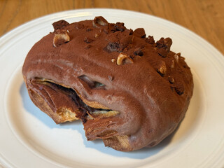 Chocolate-covered pastry with nuts on white plate. Sweetness, texture, and indulgence in artisanal dessert presentation.