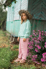 there are flowers near a wooden village house, and a child is standing next to them
