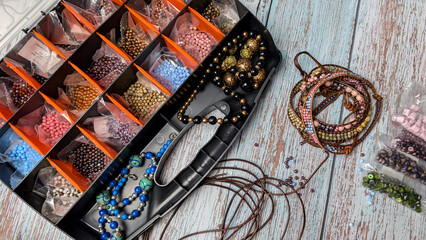 Plastic bead box with colorful beads and bracelets on the wooden table. 