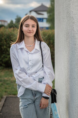Young woman with long brown hair wearing a white shirt and denim jeans stands in a lush green field, showcasing a relaxed outdoor fashion style with natural sunlight
