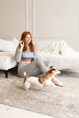 Active running dog playing with ball toy in living room with smiling woman red-haired sitting on floor. Relaxed happy time with pet at home. Playful Jack Russell terrier 
