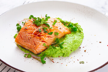 Grilled salmon filet served on a bed of green pea puree with fresh microgreens and peas, presented on a white plate