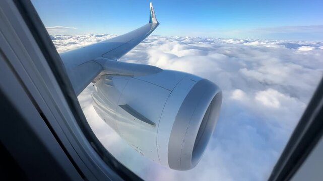Flying Above Clouds View From Airplane Window In Blue Sky. A Stunning Travel Scene Shows Airplane Wing And Jet Engine Against Blue Sky With White Clouds Below, Illuminated By Warm Sunlight.
