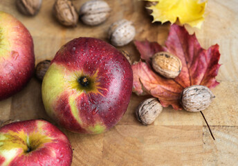 top view on bright red apples covered by water drops, walnuts on wooden background with colorful maple leaf  autumnal food