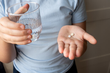 Girl is ill and stay at home. Kid holding pill and glass with water in the hands.