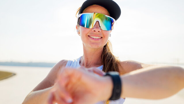 Runner checks smartwatch while smiling outdoors near a waterway on a sunny day