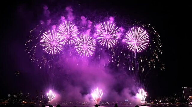 Vibrant bursts of purple fireworks lighting up the night sky above a cityscape, creating a dazzling display during a festive celebration