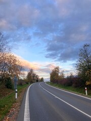 Fototapeta premium Scenic road surrounded by colorful autumn trees and fallen leaves. A peaceful fall landscape capturing the beauty of the changing season — perfect for travel, nature, and countryside photography.