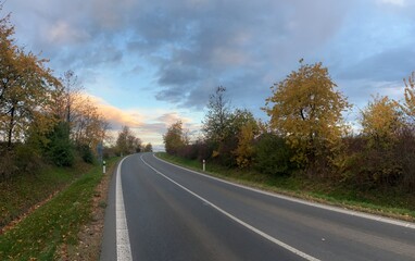 Scenic road surrounded by colorful autumn trees and fallen leaves. A peaceful fall landscape capturing the beauty of the changing season — perfect for travel, nature, and countryside photography.