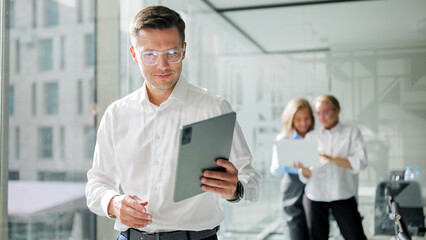 Business professional reviews data on tablet while colleagues collaborate in modern office environment