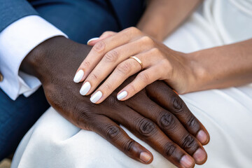 A close-up of a bride's hand resting on an African American groom's hand, displaying wedding rings