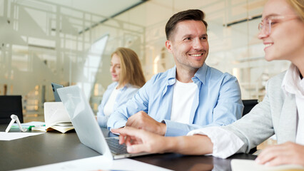 Obraz premium Group of coworkers discussing ideas while working on laptops in a modern office
