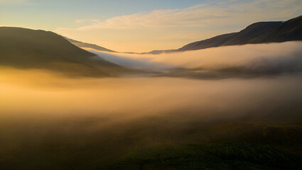 Golden mist fills a serene mountain valley at sunrise, creating a breathtaking and ethereal landscape with warm, atmospheric light.