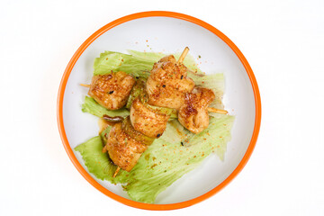 Grilled chicken skewers with spicy seasoning on lettuce, served on white plate with orange rim. Perfect for appetizer, Asian cuisine or party food.