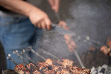 Blurred image of male hands preparing barbecue on a grill with a knife in smoke, concept of outdoor cooking and summer leisure.