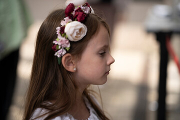 Side view waist-up photo of a little Ukrainian girl in an embroidered blouse and floral wreath outdoors with a blurred background, concept of childhood and Ukrainian tradition.