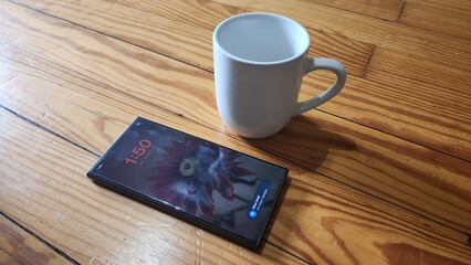 Smartphone With Flower Wallpaper Beside White Mug On Wooden Table In Morning Home Office Scene