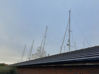 Yacht masts extending above marina building against soft blue sky, maritime minimalism.