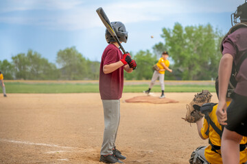 Young player waits at bat as pitcher throws baseball during a game in a local park on a cloudy afternoon © Lost_in_the_Midwest