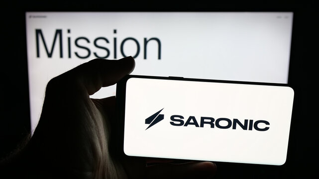 Stuttgart, Germany - 10-22-2025: Person holding mobile phone with logo of US defence company Saronic Technologies on screen in front of web page. Focus on phone display.