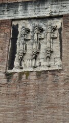Rome, Italy - 11 January 2025. A stone relief on a brick wall near the Theatre of Marcellus displays three fasces with axes, showing erosion and moss streaks across the surface.