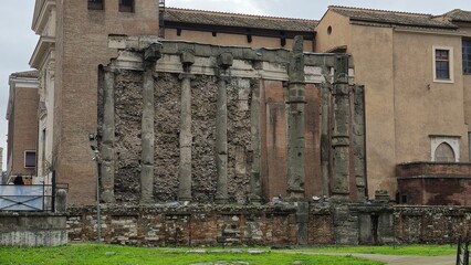 Fototapeta premium Rome, Italy - 11 January 2025. The lateral wall of San Nicola in Carcere features worn Roman columns set into crumbling masonry, framed by adjacent stuccoed structures.