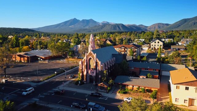 Approaching a beautiful church in Flagstaff, Arizona, USA. Amazing scenery of green cityscape and sunlit verdant mountains from drone.